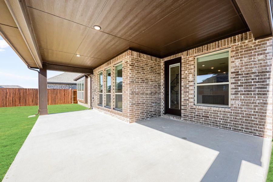 Covered back patio with concrete floor, wood ceiling, and brick exterior walls overlooking a fenced backyard
