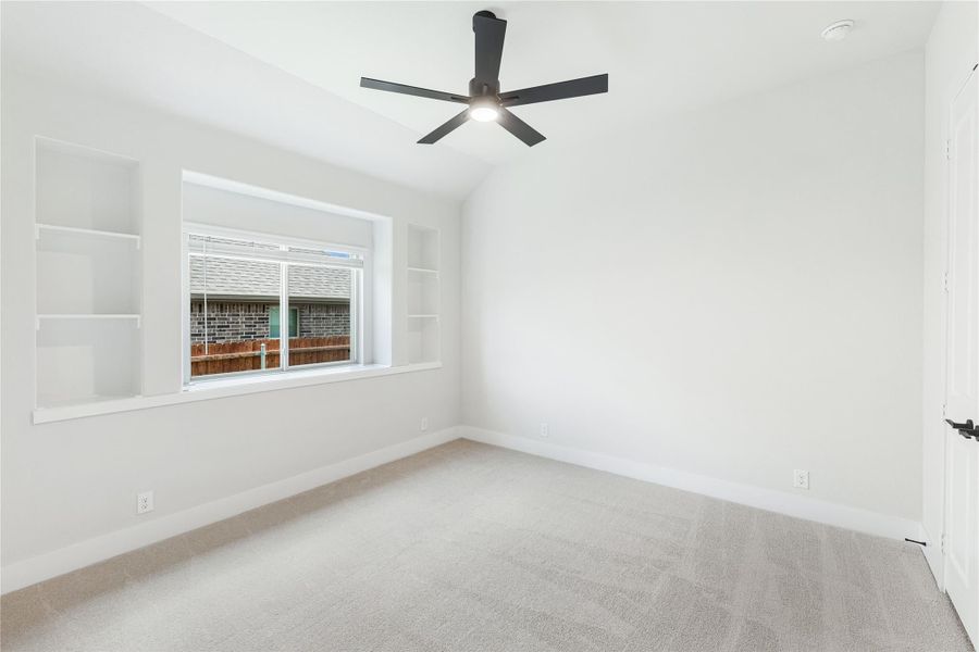 Empty bedroom with vaulted ceiling, black ceiling fan, built-in shelves, and carpet flooring Empty bedroom with vaulted ceiling, black ceiling fan, built-in shelves, and carpet flooring