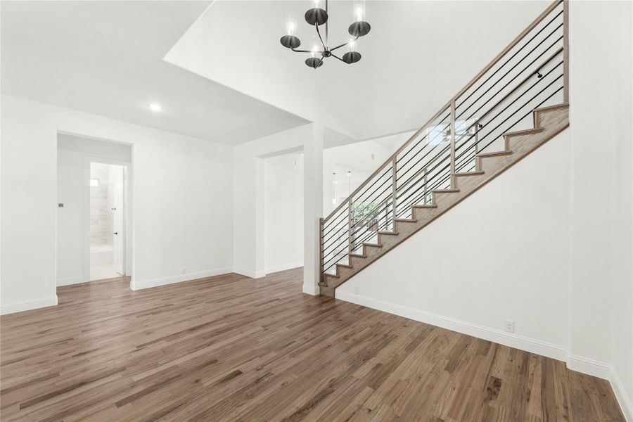 Open living area with hardwood floors, staircase with metal railing, and modern chandelier overhead