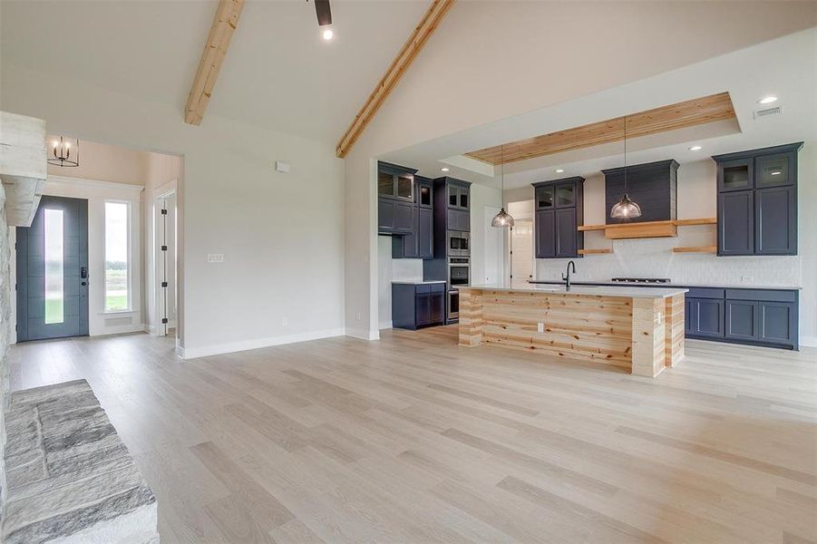 Kitchen featuring light wood-type flooring, a center island with sink, pendant lighting, sink, and tasteful backsplash