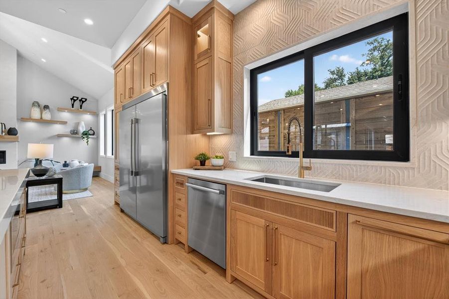 Gourmet kitchen featuring light wood cabinetry, stainless steel appliances, a deep basin sink with a gold-tone faucet, white countertops, and a textured tile backsplash Gourmet kitchen featuring light wood cabinetry, stainless steel appliances, a deep basin sink with a gold-tone faucet, white countertops, and a textured tile backsplash