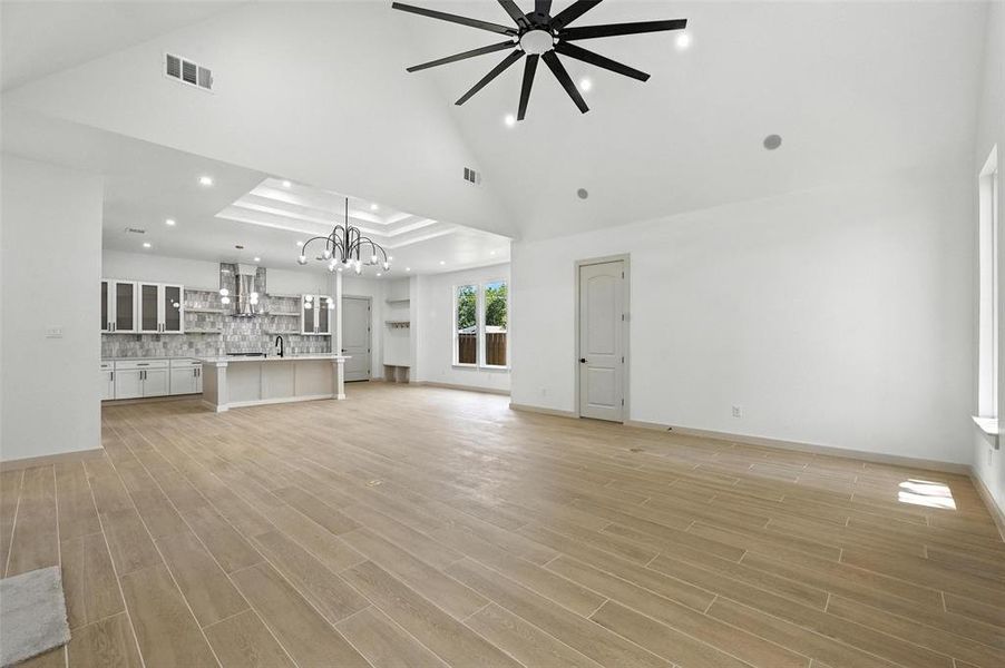 Unfurnished living room featuring recessed lighting, light wood finished floors, high vaulted ceiling, a chandelier, and a tray ceiling Unfurnished living room featuring recessed lighting, light wood finished floors, high vaulted ceiling, a chandelier, and a tray ceiling