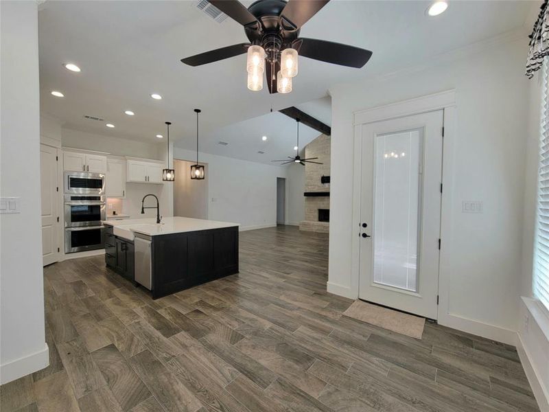 Kitchen with ceiling fan, stainless steel appliances, vaulted ceiling with beams, a center island with sink, and white cabinets