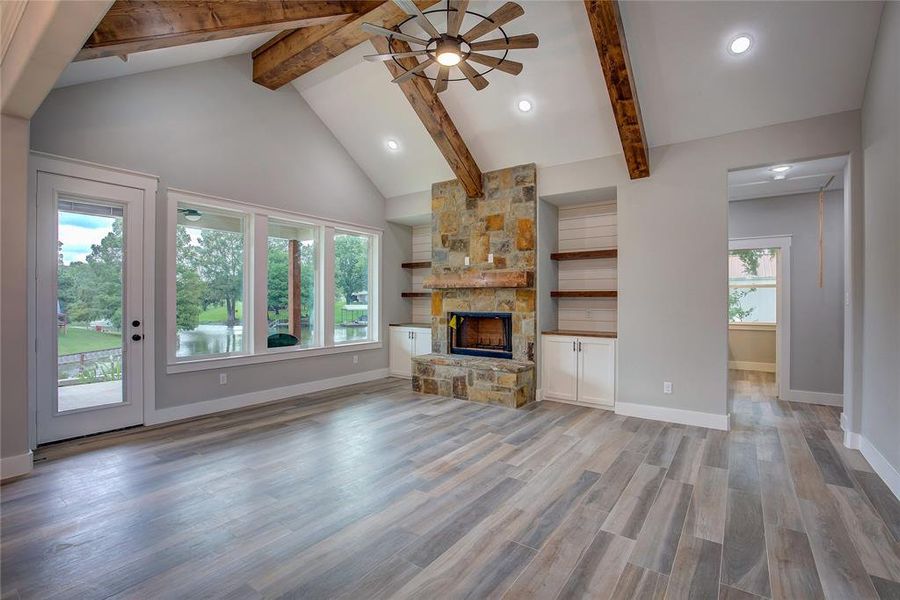Unfurnished living room featuring beam ceiling, ceiling fan, light hardwood / wood-style floors, a fireplace, and high vaulted ceiling