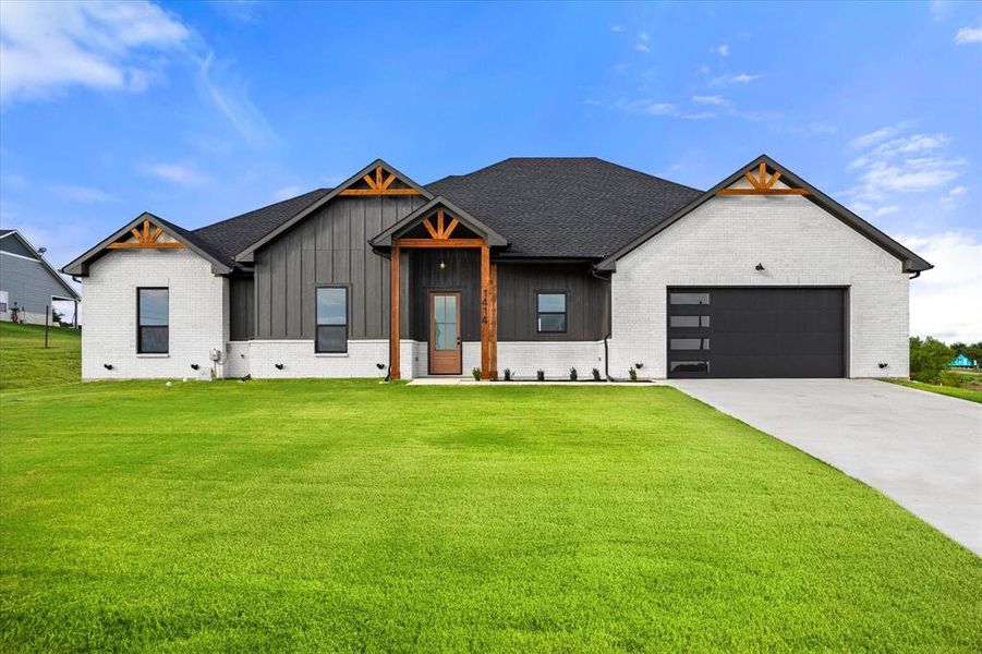 Modern farmhouse style home with an attached garage, brick siding, driveway, and a front lawn Modern farmhouse style home with an attached garage, brick siding, driveway, and a front lawn