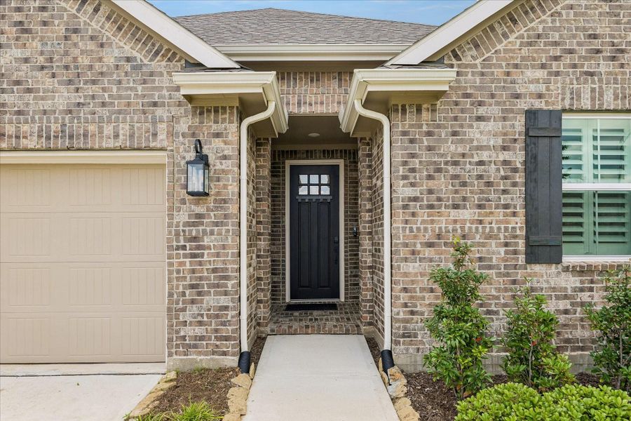 Inviting covered entry with modern farmhouse character, featuring Boral Meridian brick, statement black front door, upgraded exterior lighting, and a private recessed porch design that creates a warm welcome home.