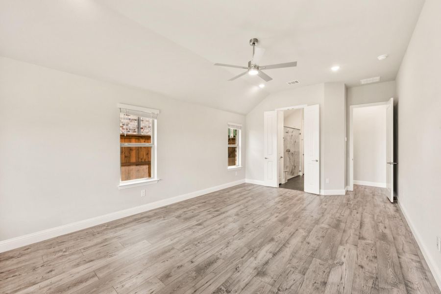 Empty bedroom with vaulted ceiling, ceiling fan, wood-look floors, and open ensuite bathroom door Empty bedroom with vaulted ceiling, ceiling fan, wood-look floors, and open ensuite bathroom door