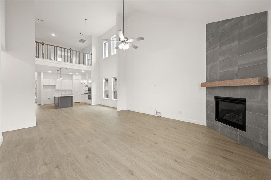 Unfurnished living room with a ceiling fan, a fireplace, light wood-style floors, a high ceiling, and a sink