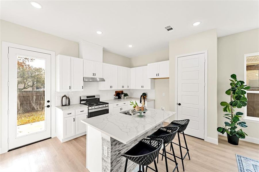 Kitchen featuring a center island with sink, white cabinetry, sink, and stainless steel stove