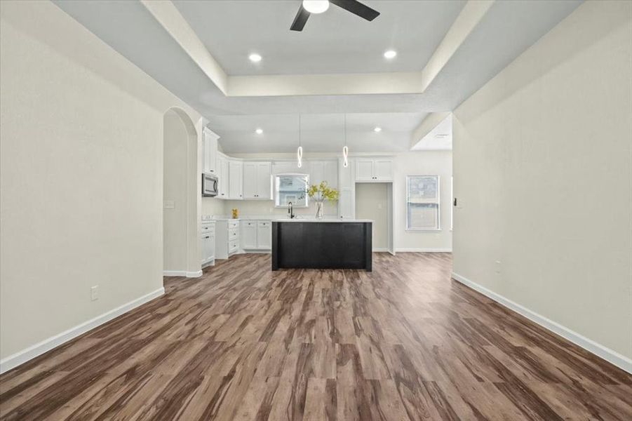 Unfurnished living room with arched walkways, dark wood-style floors, a tray ceiling, recessed lighting, and ceiling fan Unfurnished living room with arched walkways, dark wood-style floors, a tray ceiling, recessed lighting, and ceiling fan