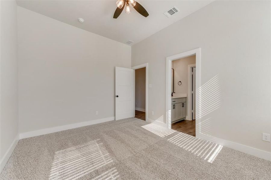 Unfurnished bedroom with carpet, ensuite bath, and ceiling fan