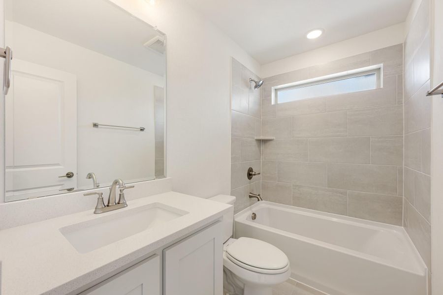 Bathroom with white vanity, quartz countertop, and tiled shower-tub combo with small window Bathroom with white vanity, quartz countertop, and tiled shower-tub combo with small window