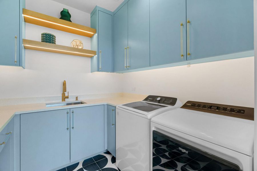 Laundry space featuring light blue cabinetry, built-in sink with brass-finish faucet, under-cabinet lighting, and illuminated wood-finish shelving