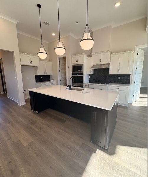 Two tone kitchen with decorative backsplash, a high ceiling, two tone cabinetry, a large island, and stainless steel appliances
