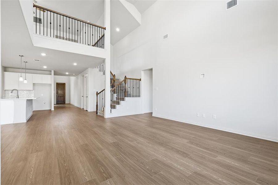 Unfurnished living room with recessed lighting, light wood-style flooring, stairway, and a high ceiling Unfurnished living room with recessed lighting, light wood-style flooring, stairway, and a high ceiling