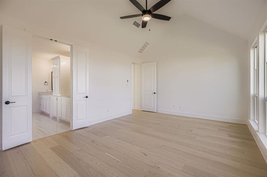Unfurnished bedroom with light wood-type flooring, ceiling fan, high vaulted ceiling, and ensuite bath Unfurnished bedroom with light wood-type flooring, ceiling fan, high vaulted ceiling, and ensuite bath