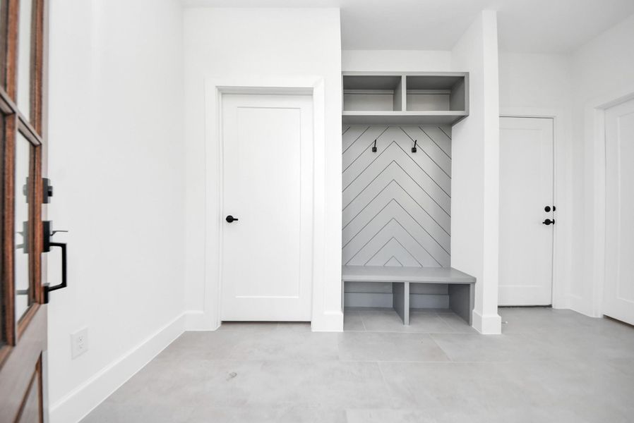 A functional and stylish entryway featuring clean white walls, a chevron-patterned accent wall, built-in bench, and open shelving—creating an organized, welcoming space for everyday living.