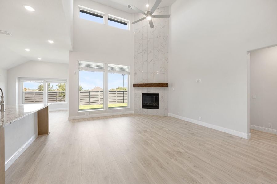 Open living area with two-story ceiling, marble tile fireplace, ceiling fan, and light wood floors
