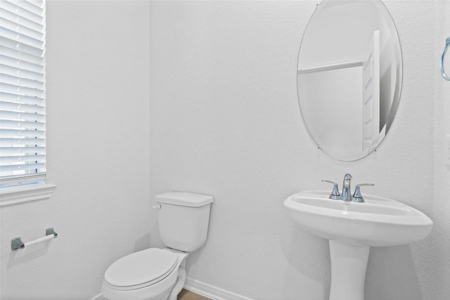 The powder room on the first floor includes a window with privacy blinds, pedestal sink, mirror, and toilet to conveniently meet your needs. The powder room on the first floor includes a window with privacy blinds, pedestal sink, mirror, and toilet to conveniently meet your needs.