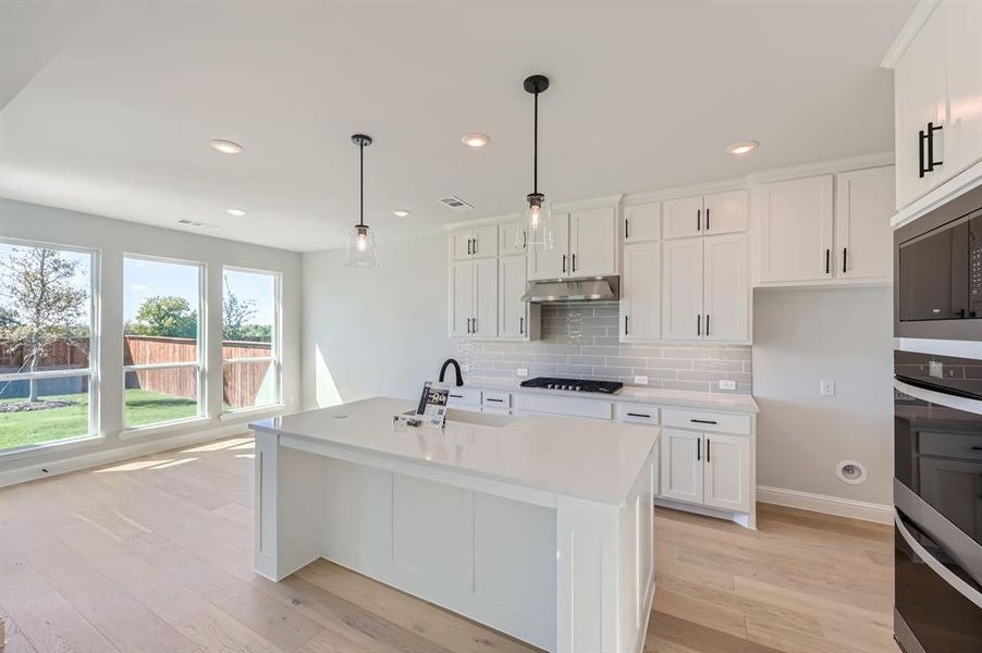 Kitchen featuring white cabinets, light hardwood / wood-style floors, hanging light fixtures, and a kitchen island with sink