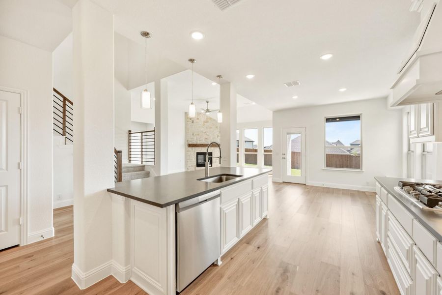 Kitchen island with dark countertop, sink, and stainless dishwasher, white cabinets, and light wood floors open to living area. Kitchen island with dark countertop, sink, and stainless dishwasher, white cabinets, and light wood floors open to living area.