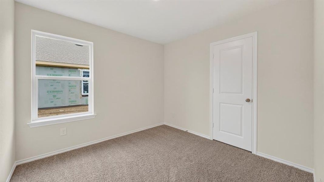 Light-filled interior space featuring neutral wall paint, gray carpet, a white two-panel door, and a white-framed window