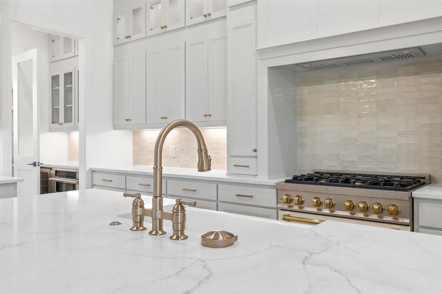 Kitchen featuring decorative backsplash, light stone countertops, stainless steel range, and white cabinets