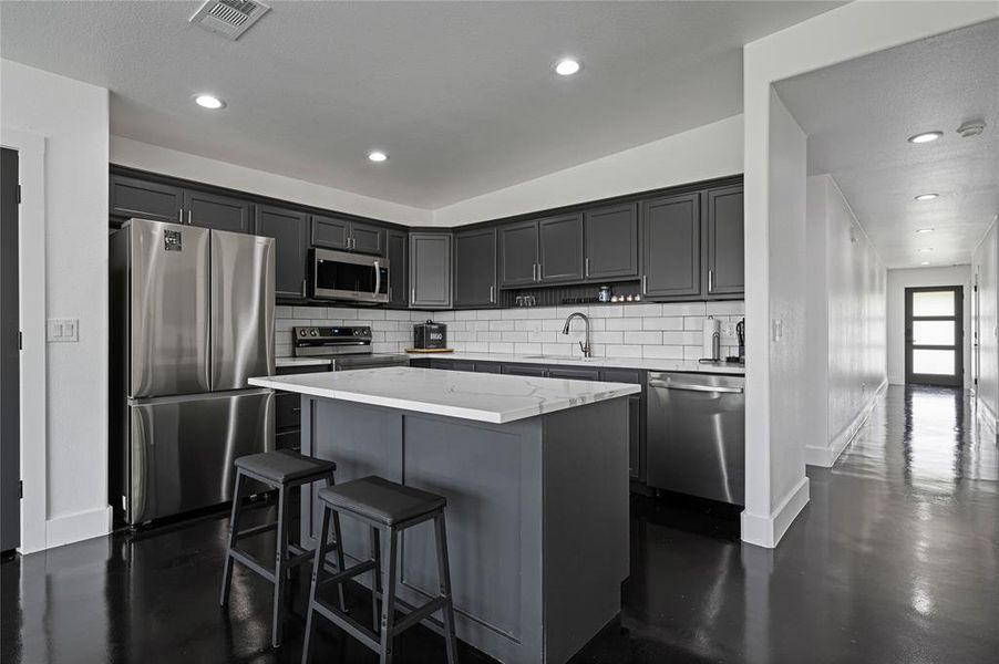 Kitchen featuring tasteful backsplash, light stone counters, stainless steel appliances, a kitchen island, and sink