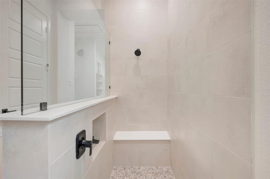 The shower features light-colored tile walls, a built-in bench, and a dark-toned shower head