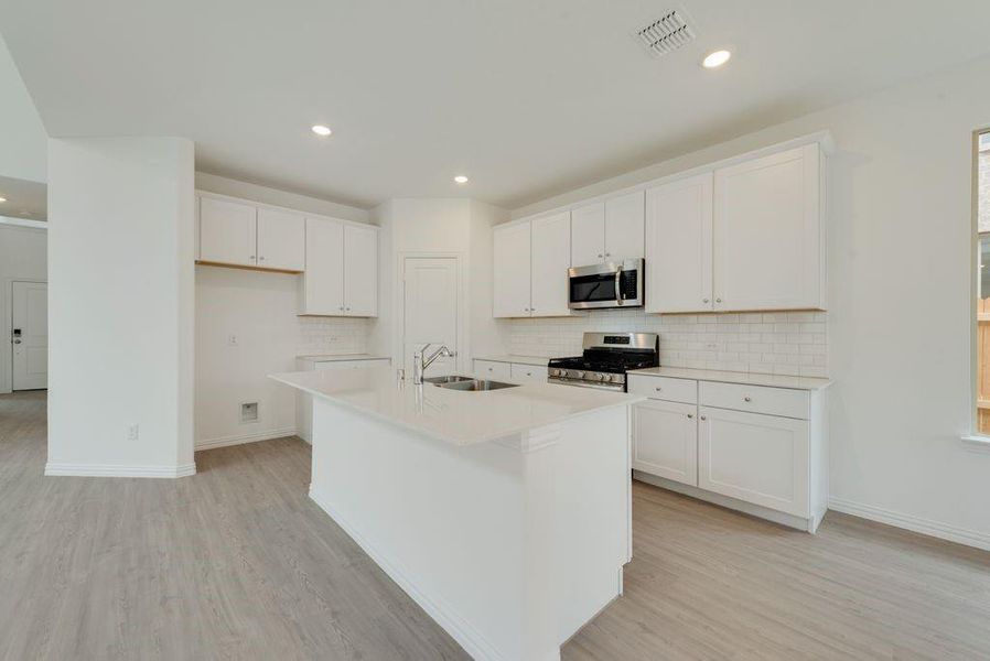 Kitchen with stainless steel appliances, light wood-type flooring, decorative backsplash, white cabinets, and a kitchen island with sink Kitchen with stainless steel appliances, light wood-type flooring, decorative backsplash, white cabinets, and a kitchen island with sink