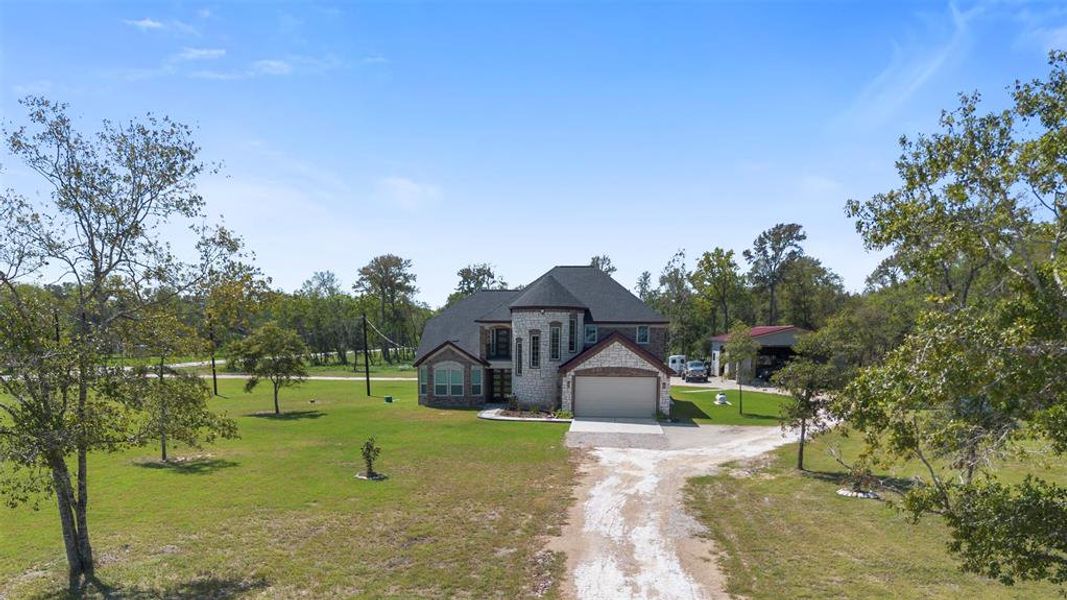 This photo showcases a spacious two-story stone house with a sizable front yard and a long driveway. The property is surrounded by trees, offering a serene, private setting.