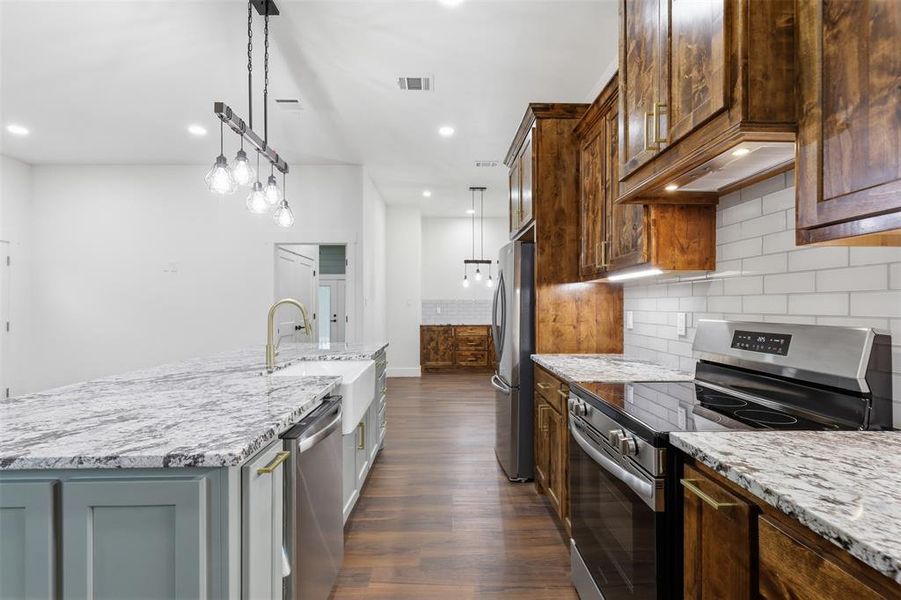 Kitchen featuring a granite island with an undermount farmhouse sink, stainless steel dishwasher, and gold-finish faucet Kitchen featuring a granite island with an undermount farmhouse sink, stainless steel dishwasher, and gold-finish faucet