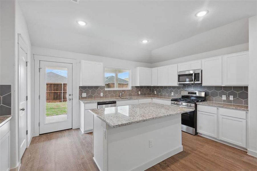 Kitchen with a sink, a kitchen island, appliances with stainless steel finishes, white cabinets, and light wood-style floors Kitchen with a sink, a kitchen island, appliances with stainless steel finishes, white cabinets, and light wood-style floors
