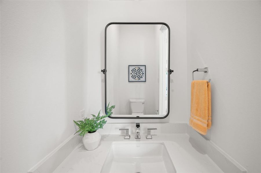 This elegant powder room features quartz surfaces, and contemporary fixtures that elevate the space with a refined designer touch.