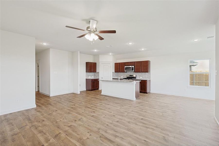 Kitchen with ceiling fan, an island with sink, appliances with stainless steel finishes, tasteful backsplash, and light hardwood / wood-style floors