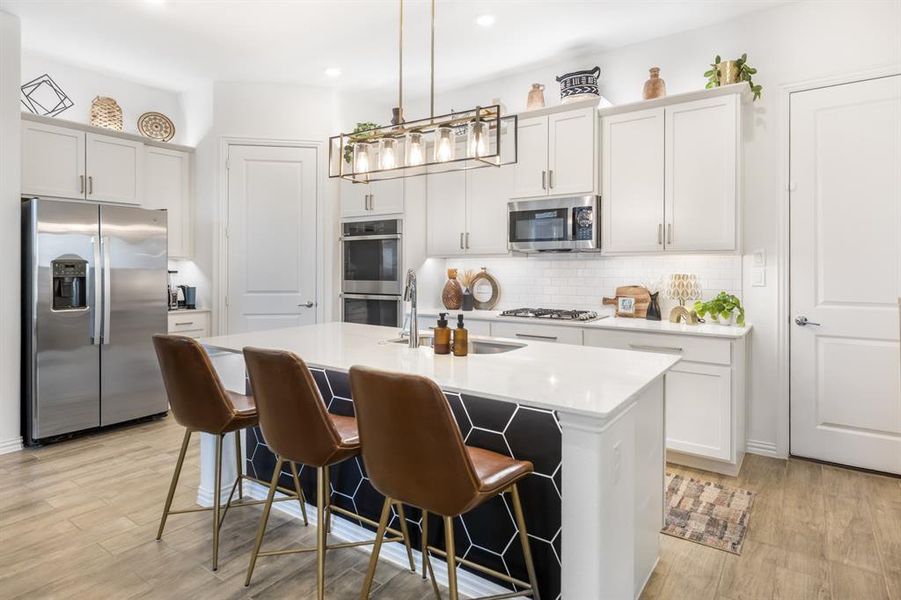 Kitchen with appliances with stainless steel finishes, a breakfast bar area, pendant lighting, a kitchen island with sink, and light wood-style floors Kitchen with appliances with stainless steel finishes, a breakfast bar area, pendant lighting, a kitchen island with sink, and light wood-style floors