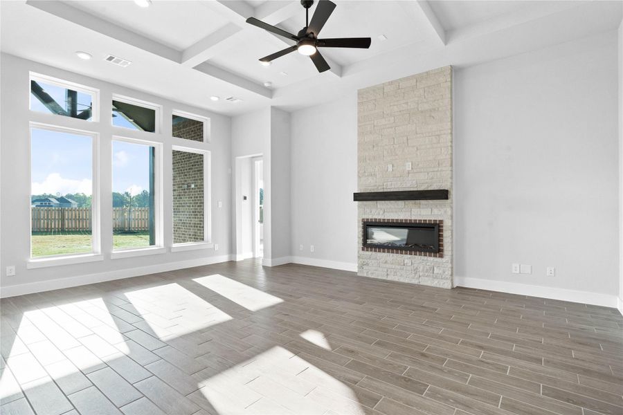 A stately floor-to-ceiling stone fireplace serves as the room's focal point, featuring a sleek linear gas insert and a rustic dark-wood mantel. The architectural interest continues overhead with a grand coffered ceiling, accented by integrated LED lighting and a contemporary black ceiling fan. A stately floor-to-ceiling stone fireplace serves as the room's focal point, featuring a sleek linear gas insert and a rustic dark-wood mantel. The architectural interest continues overhead with a grand coffered ceiling, accented by integrated LED lighting and a contemporary black ceiling fan.
