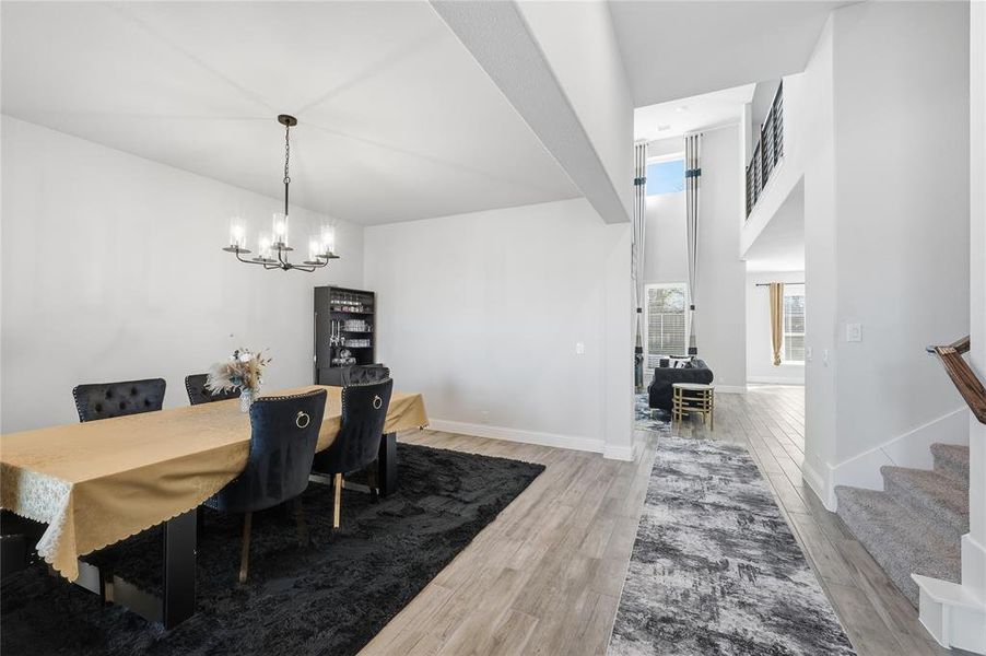 Dining room with stairs, light wood-type flooring, a chandelier, and a high ceiling
