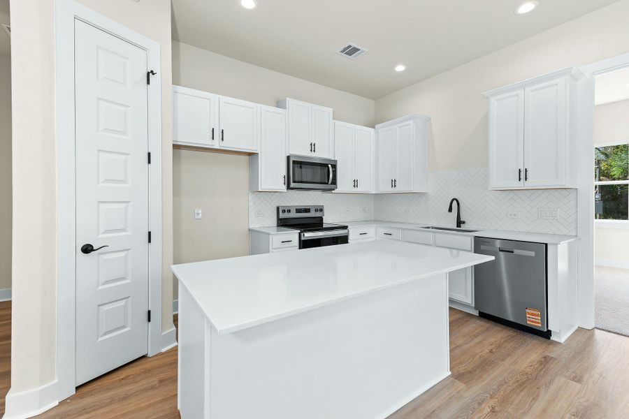 Kitchen featuring white cabinetry, appliances with stainless steel finishes, tasteful backsplash, light wood-type flooring, and a center island