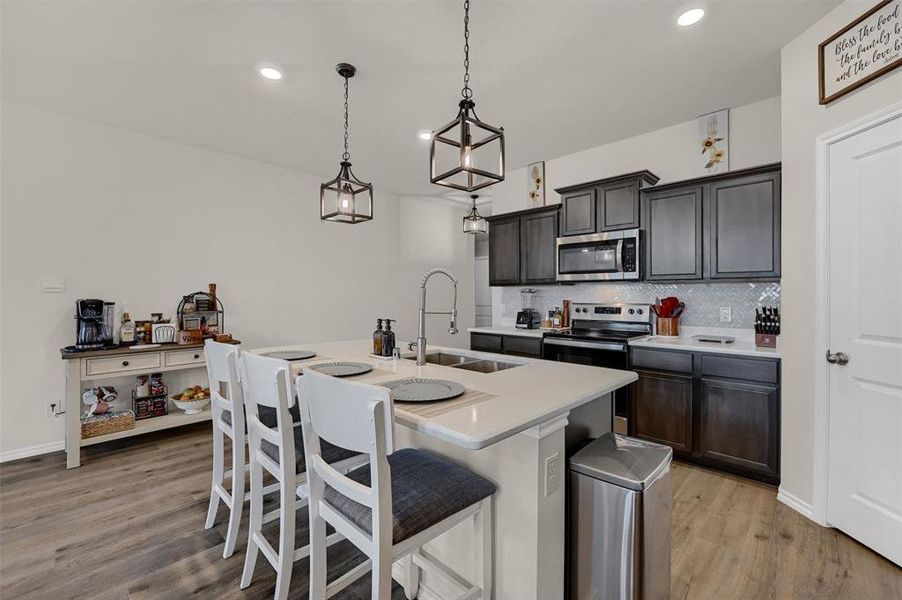 Kitchen featuring light countertops, backsplash, a sink, light wood-style flooring, and appliances with stainless steel finishes
