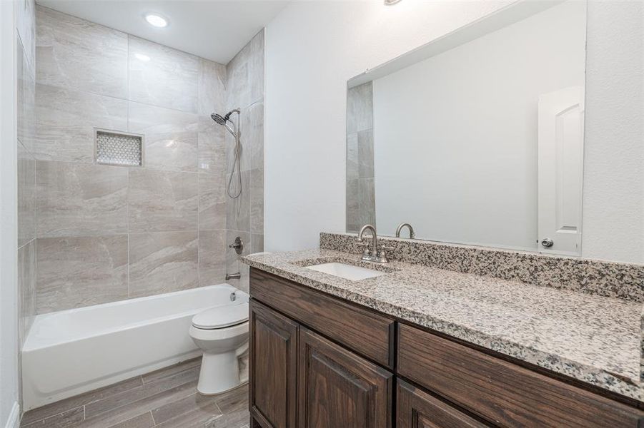 Bathroom featuring washtub / shower combination, wood finish floors, vanity, and toilet