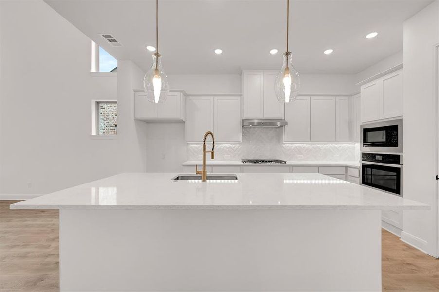 Kitchen with light wood-style flooring, white cabinets, light stone countertops, and a center island with sink