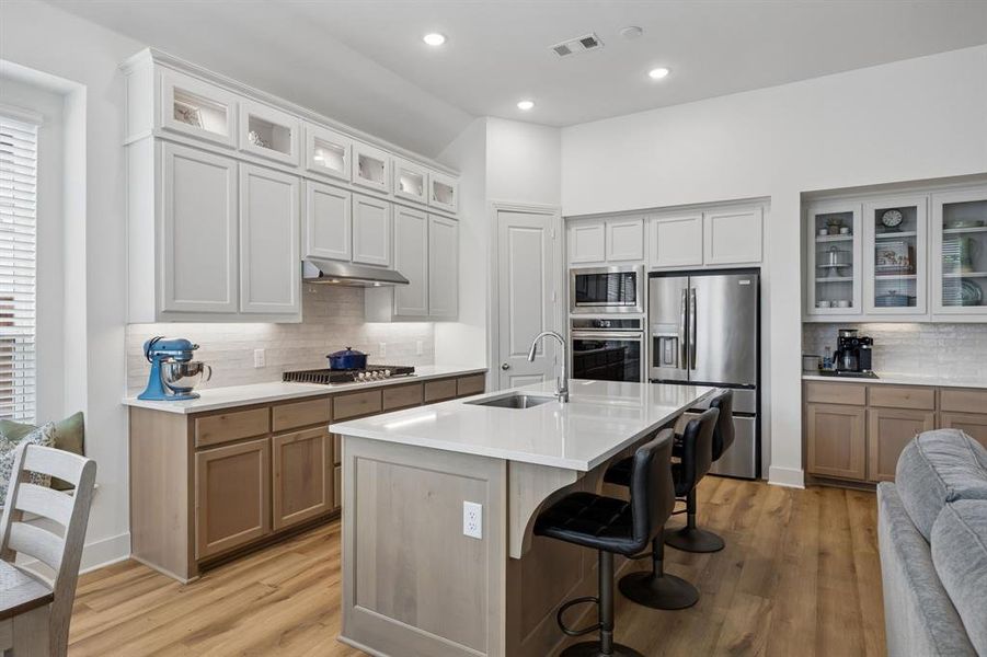 Open-concept kitchen featuring light-toned cabinetry, a spacious center island with seating, stainless steel appliances, and wood-finish flooring