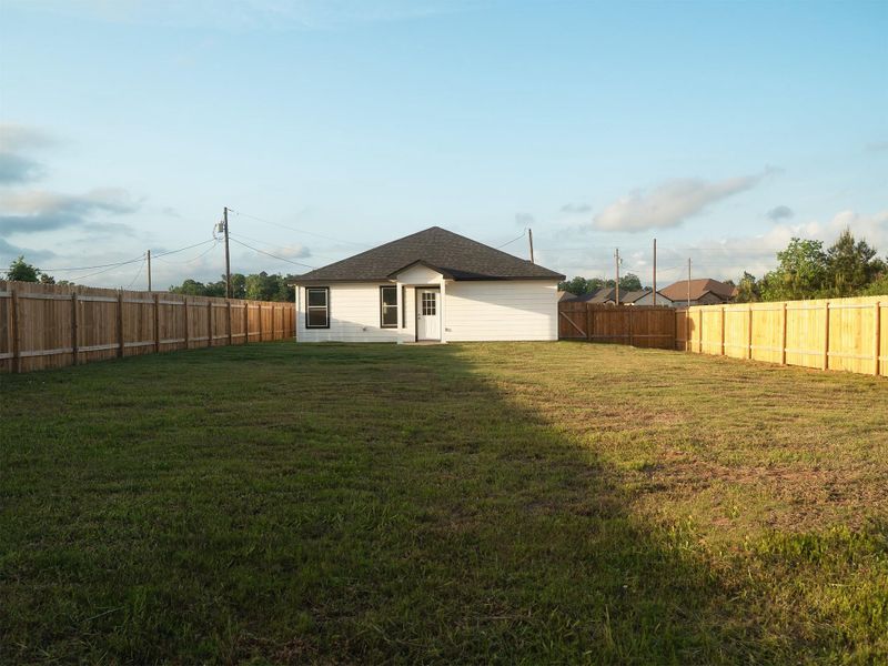 Spacious, fenced-in backyard. The yard is grassy, flat, and bordered by a tall wooden fence, offering privacy and ample outdoor space.