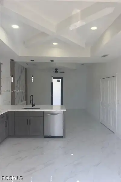 Coffered ceiling with recessed lighting, large-format tile flooring, gray cabinetry with stone-finish countertops, stainless steel dishwasher, and matte black plumbing fixtures Coffered ceiling with recessed lighting, large-format tile flooring, gray cabinetry with stone-finish countertops, stainless steel dishwasher, and matte black plumbing fixtures