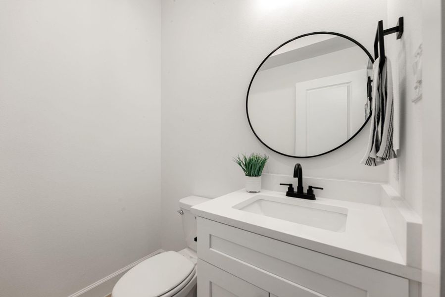 Stylish powder room showcasing a sleek white vanity with solid surface countertop, black hardware, and a round statement mirror. Bright, modern, and thoughtfully designed for everyday convenience and guests.