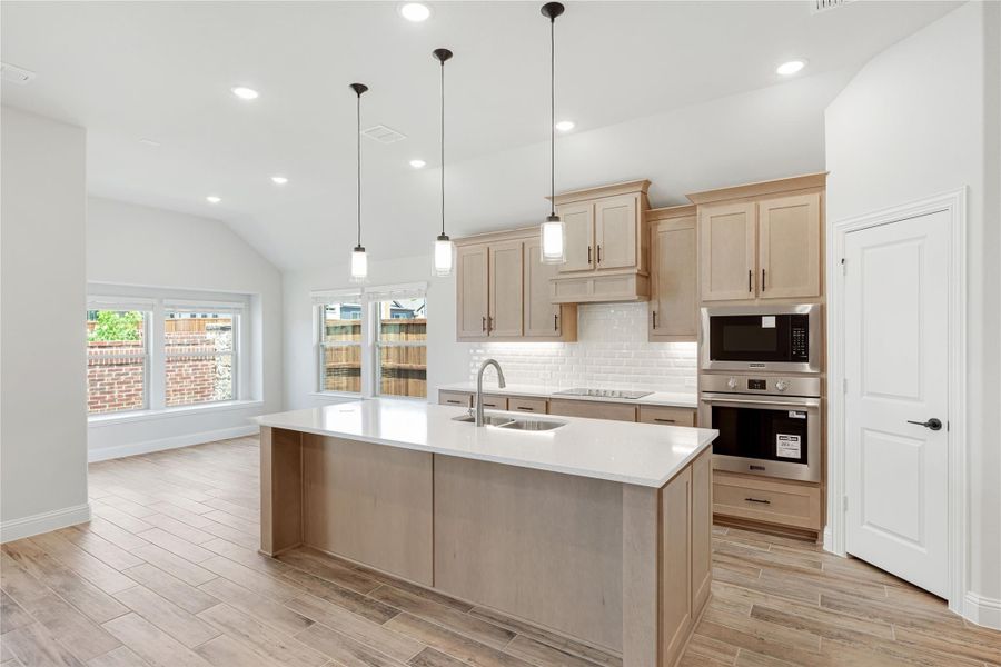 Kitchen with large center island, light wood cabinets, white countertops, subway tile backsplash, and stainless steel appliances