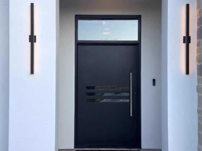 A modern black front door with a glass transom welcomes visitors to this home. A modern black front door with a glass transom welcomes visitors to this home.