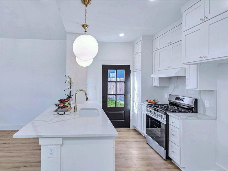 Kitchen featuring white cabinetry, a sink, stainless steel gas range, light wood-type flooring, and under cabinet range hood