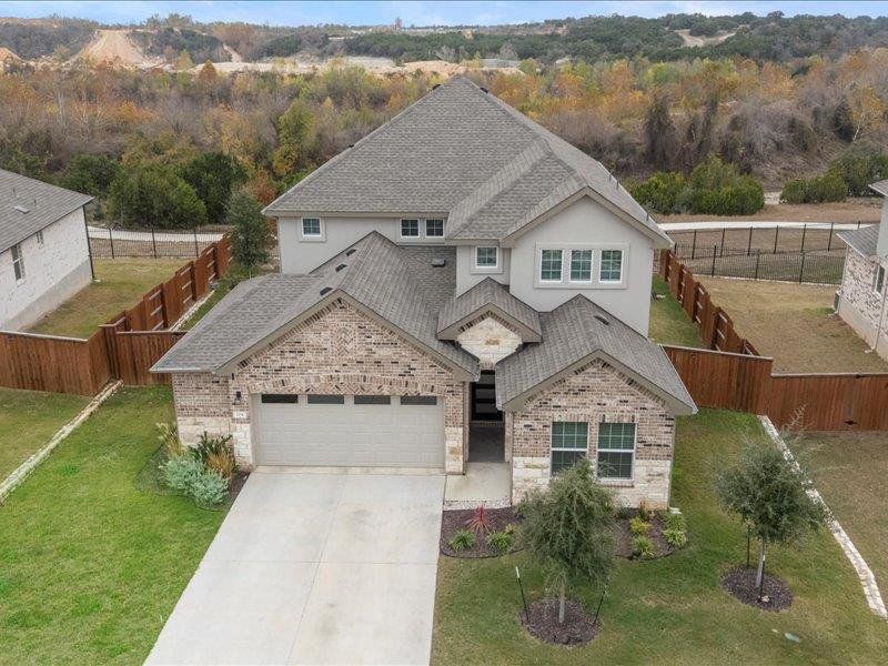 View of front of home featuring a shingled roof, concrete driveway, a garage, brick siding, and a fenced backyard